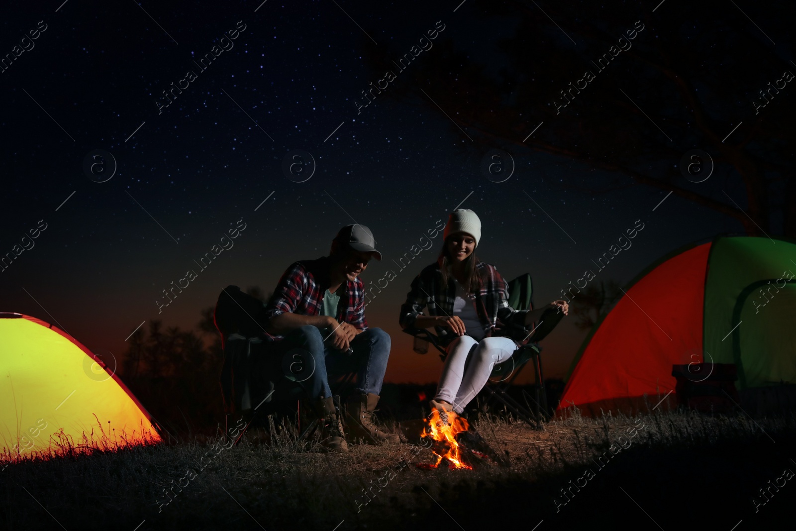 Photo of Couple near bonfire at night. Camping season