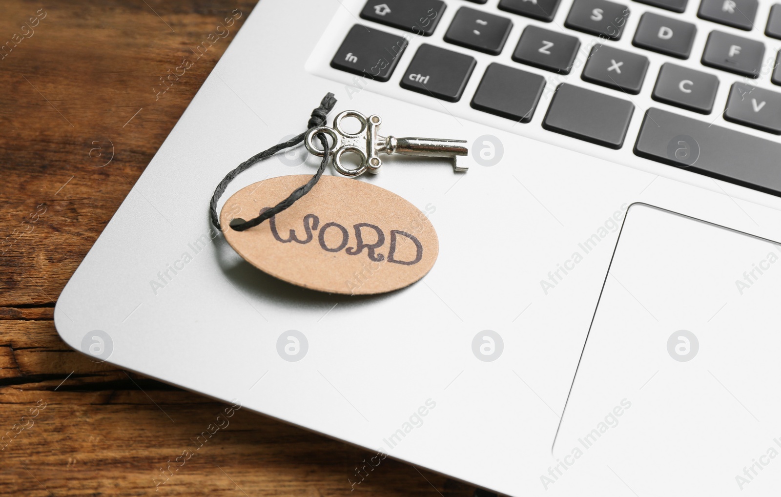 Photo of Vintage key with tag and laptop on wooden table, closeup. Keyword concept