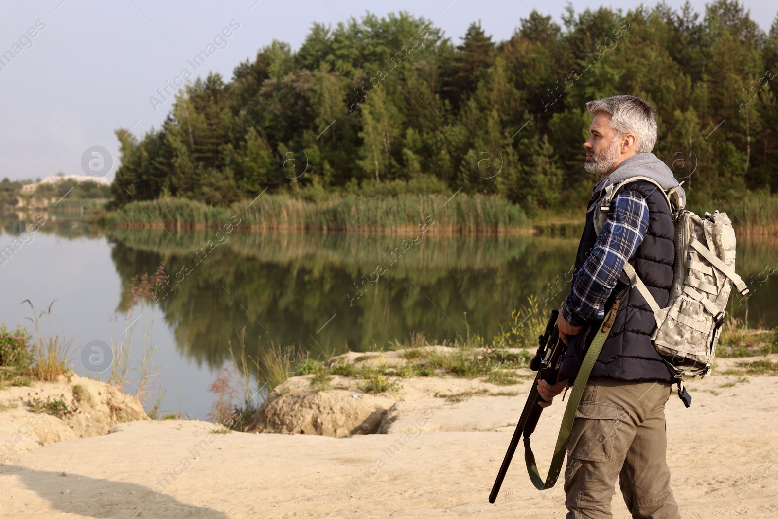 Photo of Man with hunting rifle near lake outdoors. Space for text