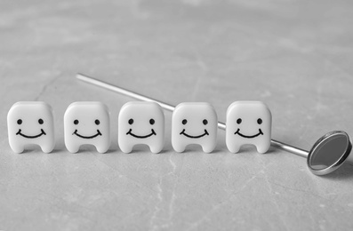 Photo of Decorative teeth and dentist mirror on grey table, closeup