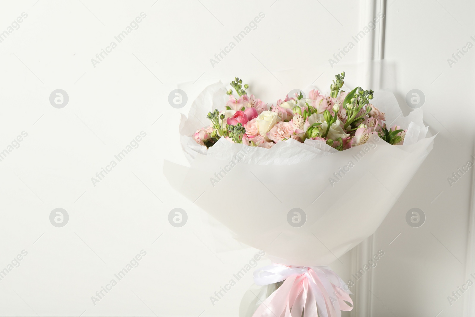 Photo of Beautiful bouquet of fresh flowers near white wall, space for text