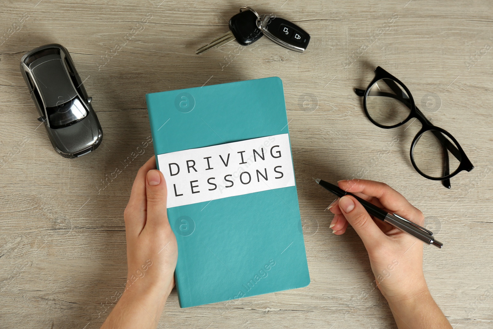 Photo of Woman with workbook for driving lessons and car key at wooden table, top view. Passing license exam