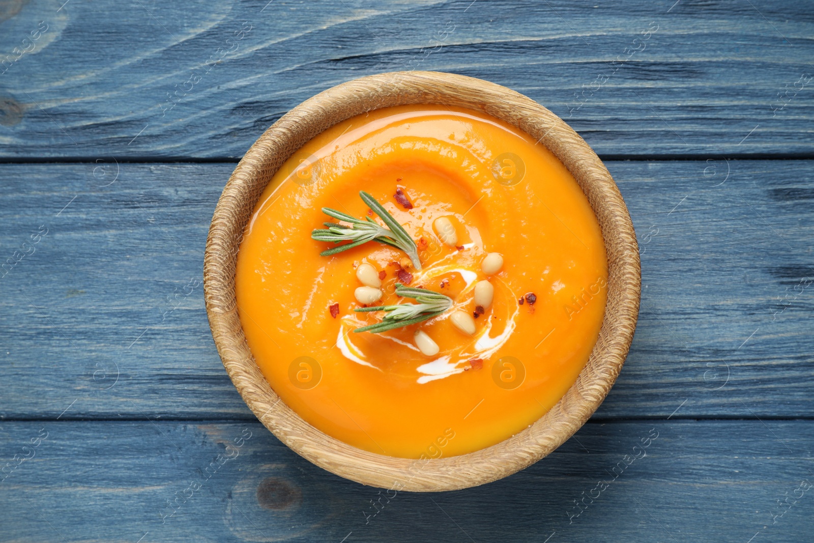 Photo of Delicious pumpkin soup in bowl on blue wooden table, top view