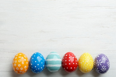 Photo of Flat lay composition of painted Easter eggs on wooden table, space for text