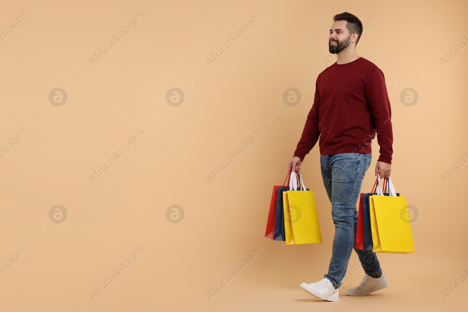 Photo of Smiling man with many paper shopping bags on beige background. Space for text