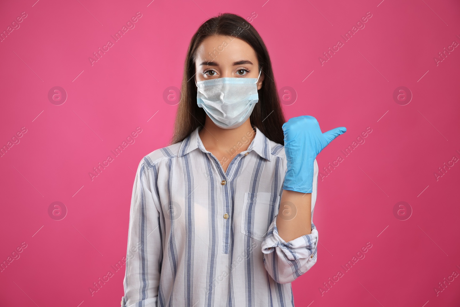 Photo of Woman in protective face mask and medical gloves pointing at something on pink background
