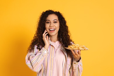 Photo of Excited African American woman with French fries on yellow background