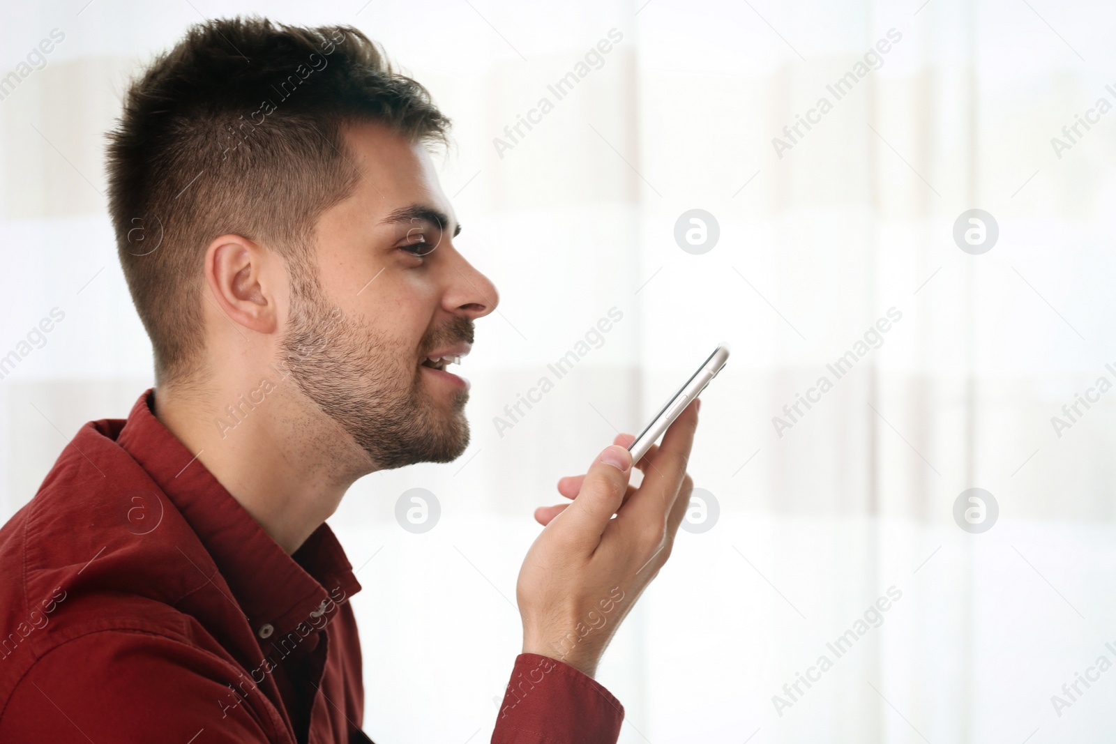 Photo of Young man using voice search on smartphone indoors