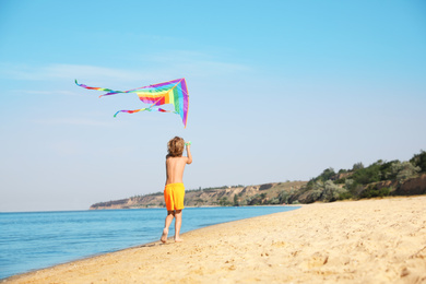 Photo of Cute little child with kite running at beach on sunny day
