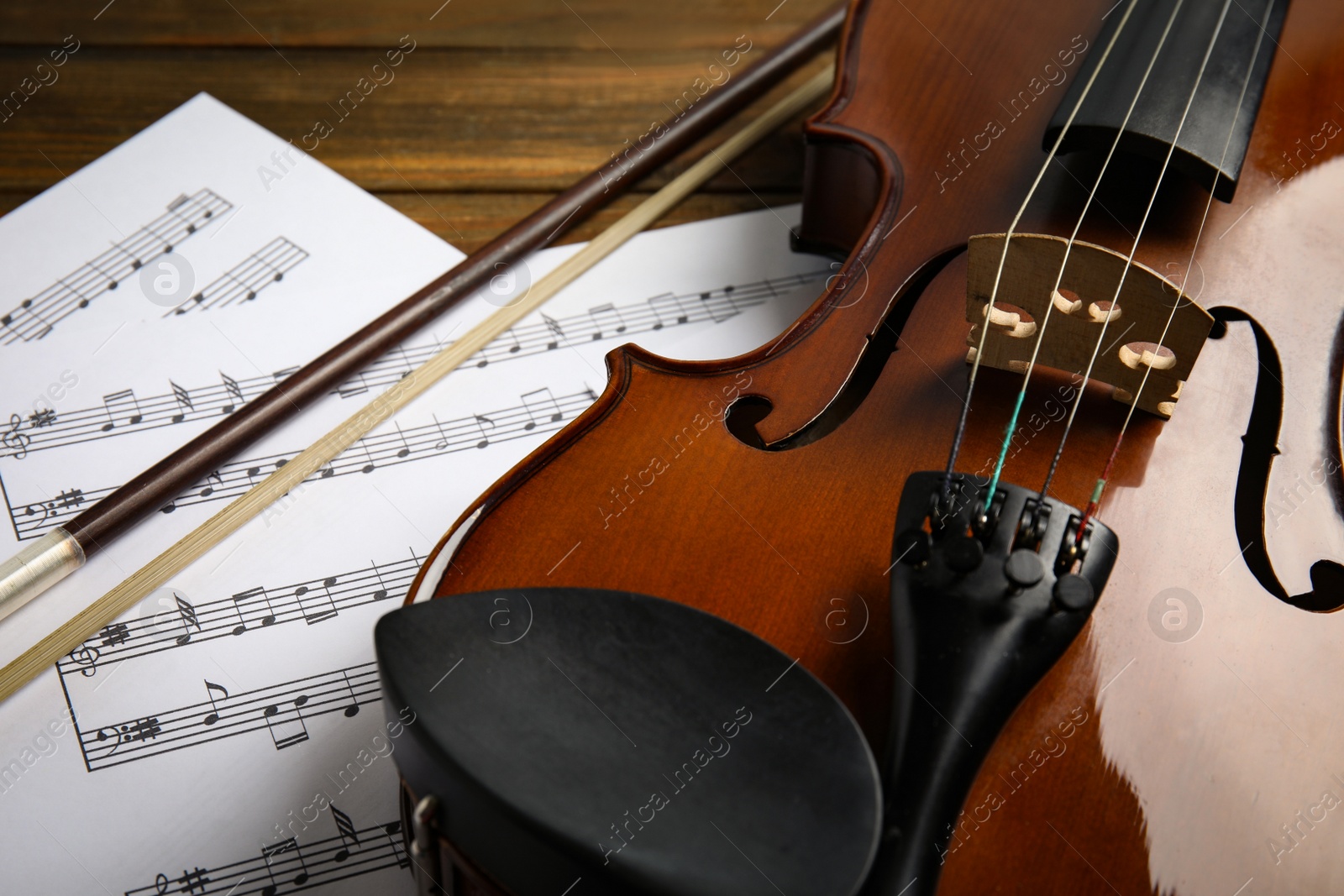 Photo of Beautiful violin, bow and note sheets on wooden table, closeup