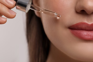 Photo of Woman applying essential oil onto face on light grey background, closeup