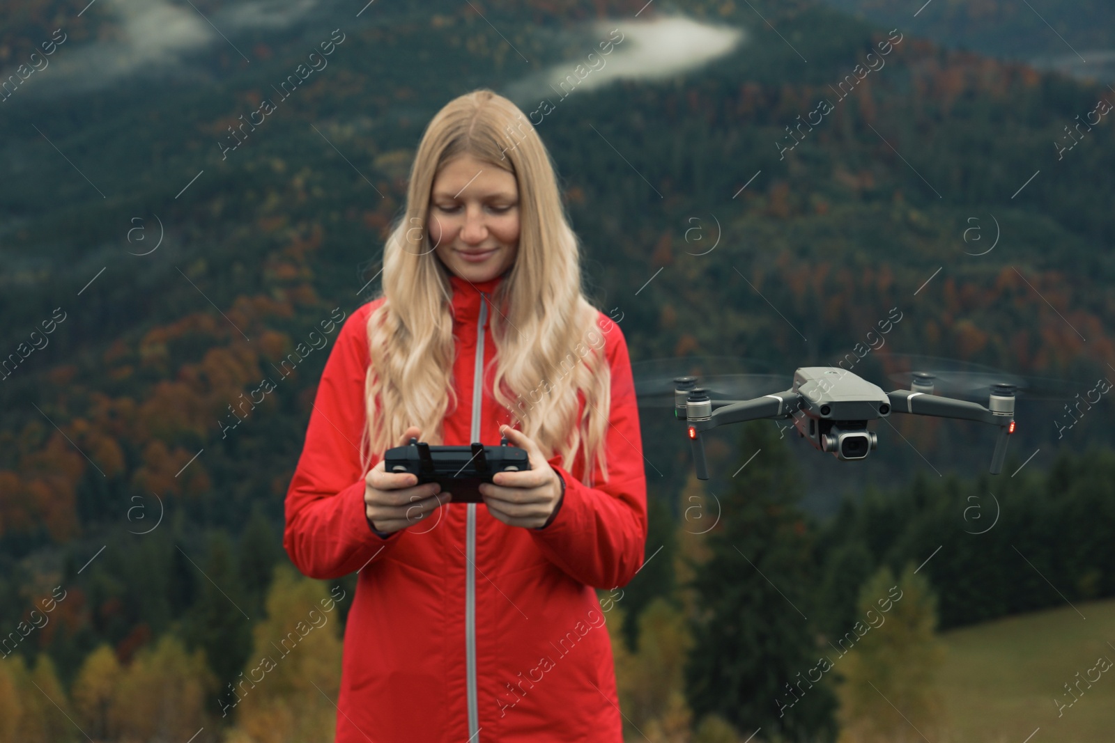 Photo of Young woman operating modern drone with remote control in mountains