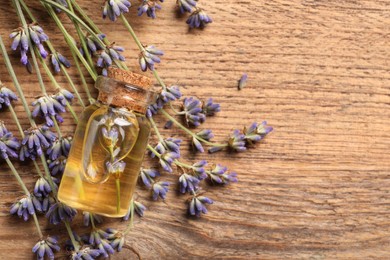 Bottle of essential oil and lavender flowers on wooden table, flat lay. Space for text