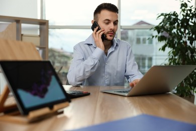 Photo of Forex trader talking on phone while working with laptop in office