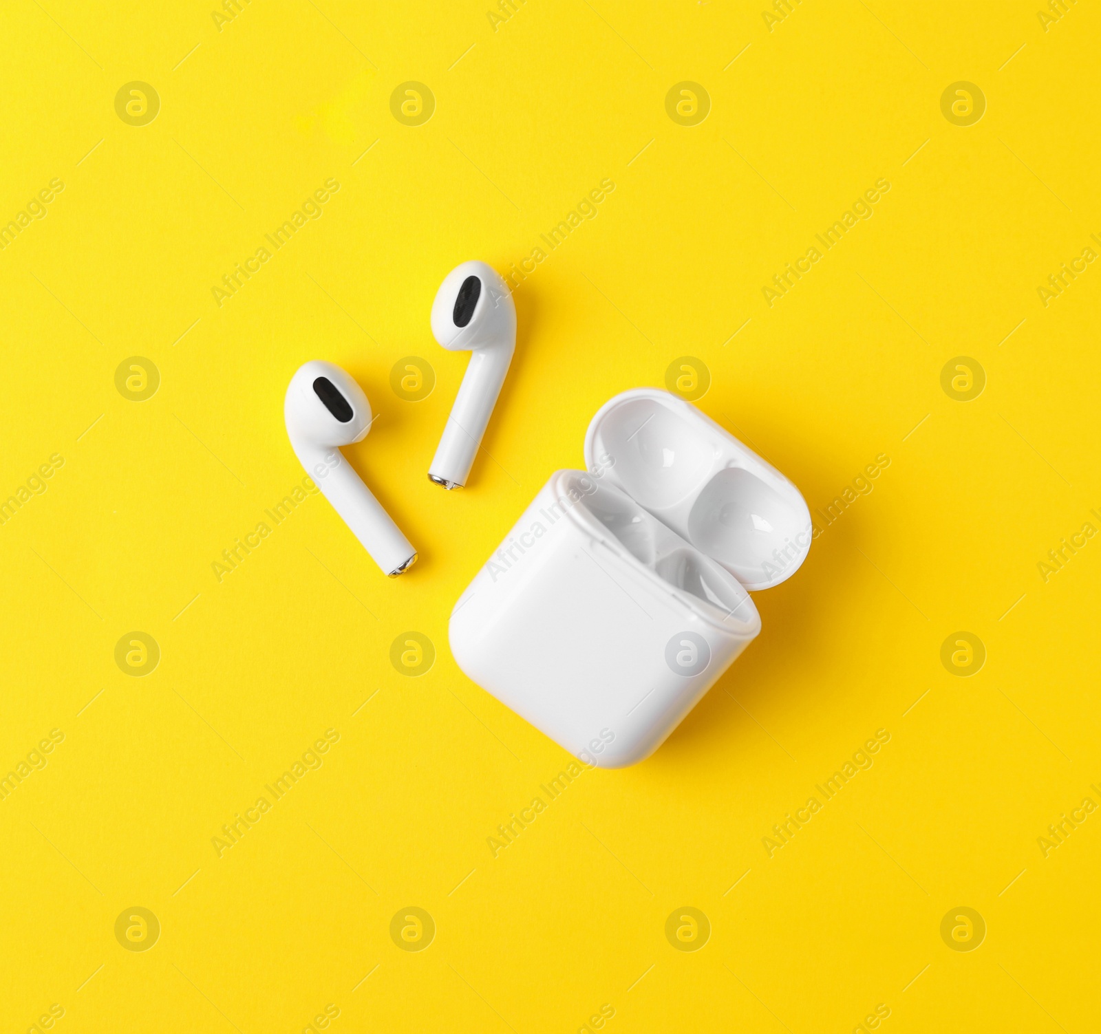 Photo of Modern wireless earphones and charging case on yellow background, flat lay