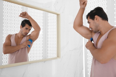 Photo of Handsome young man applying deodorant in bathroom