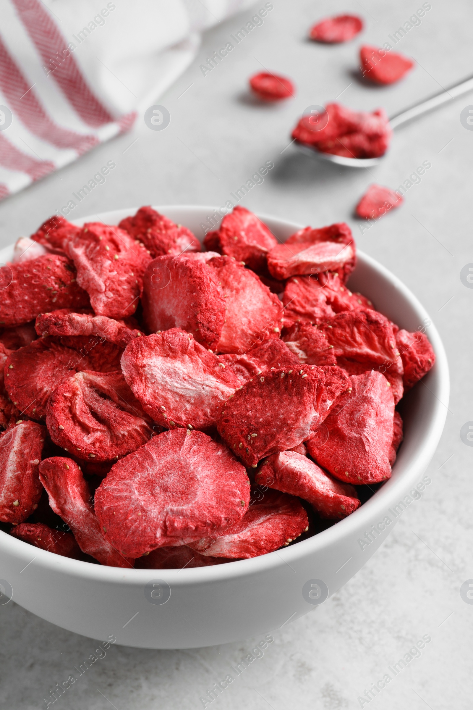 Photo of Bowl with dried strawberries on light grey table, closeup