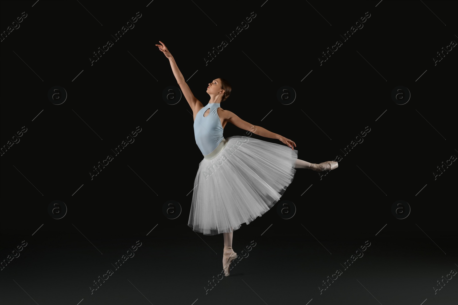 Photo of Young ballerina practicing dance moves on black background