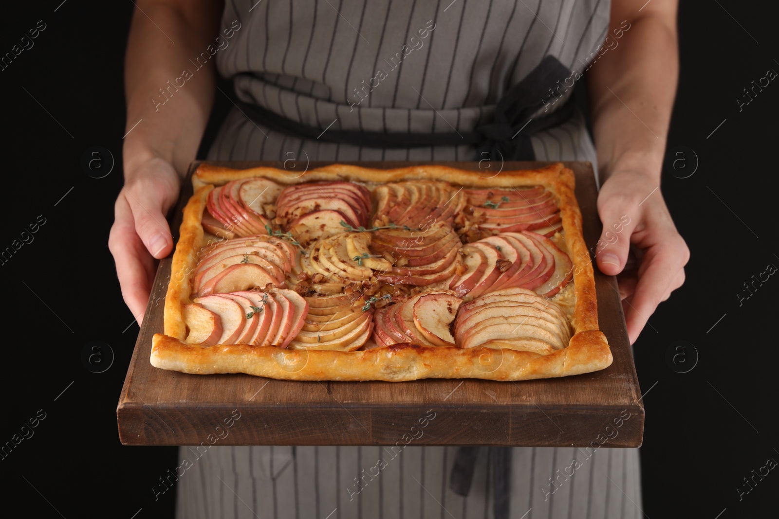 Photo of Woman holding freshly baked apple pie with nuts on black background, closeup