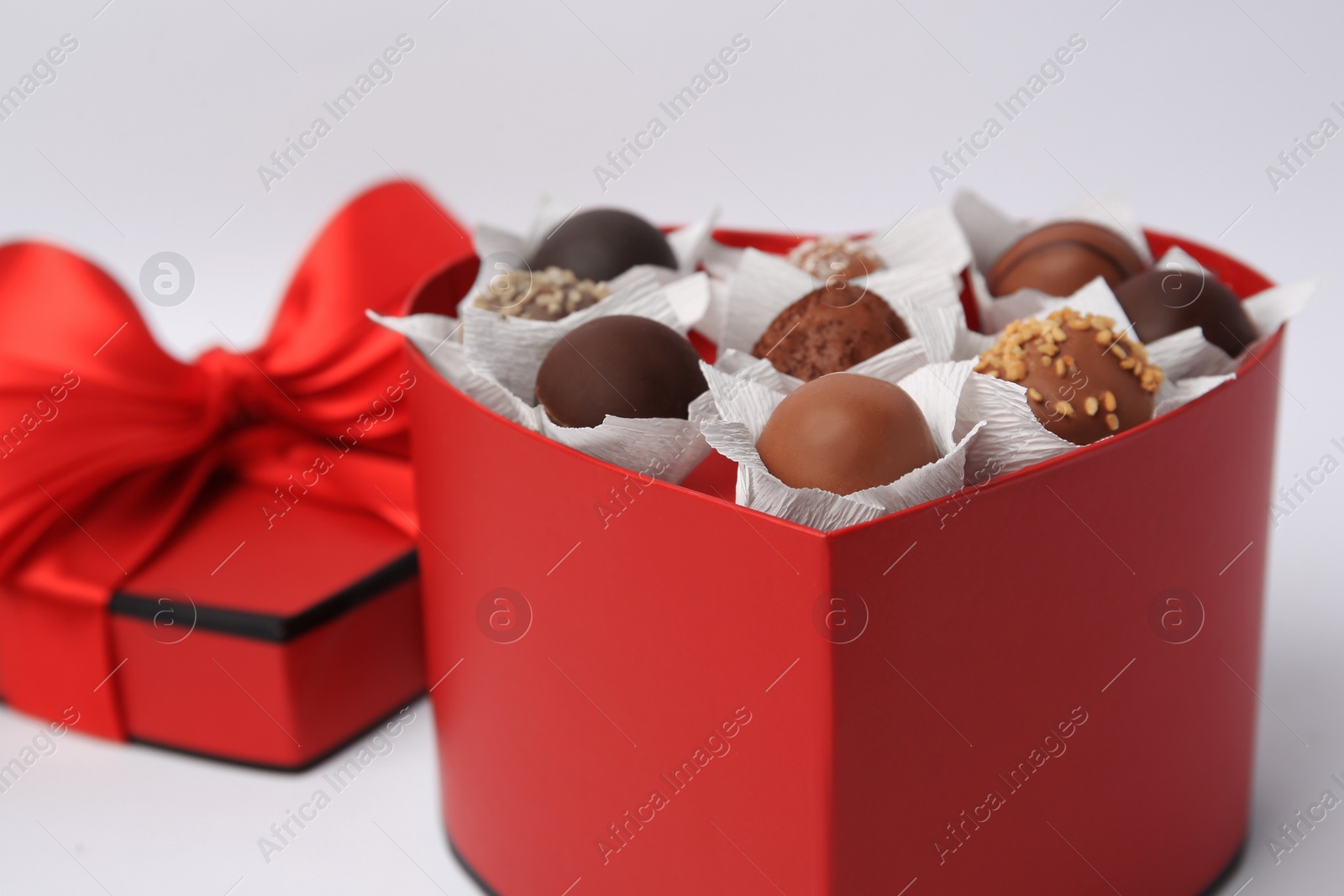 Photo of Heart shaped box with delicious chocolate candies on white background, closeup