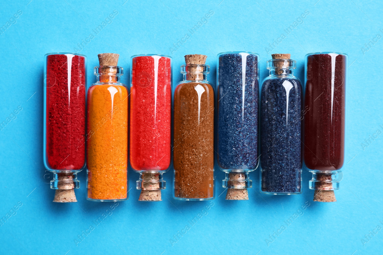 Photo of Glass bottles with different food coloring on light blue background, flat lay