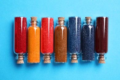 Glass bottles with different food coloring on light blue background, flat lay