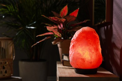 Photo of Himalayan salt lamp on wooden table near brown wall indoors