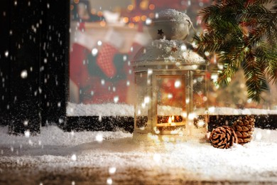 Image of Snow falling onto window sill with Christmas lantern outdoors