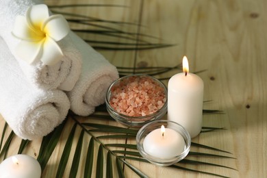 Photo of Spa composition. Rolled towels, sea salt and burning candles on wooden table, space for text