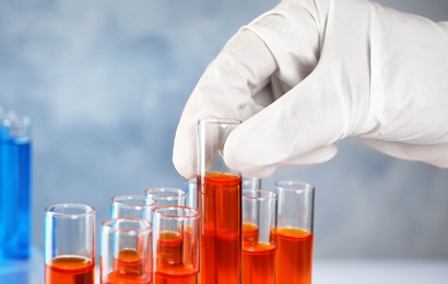 Scientist taking test tube with liquid sample on grey background, closeup