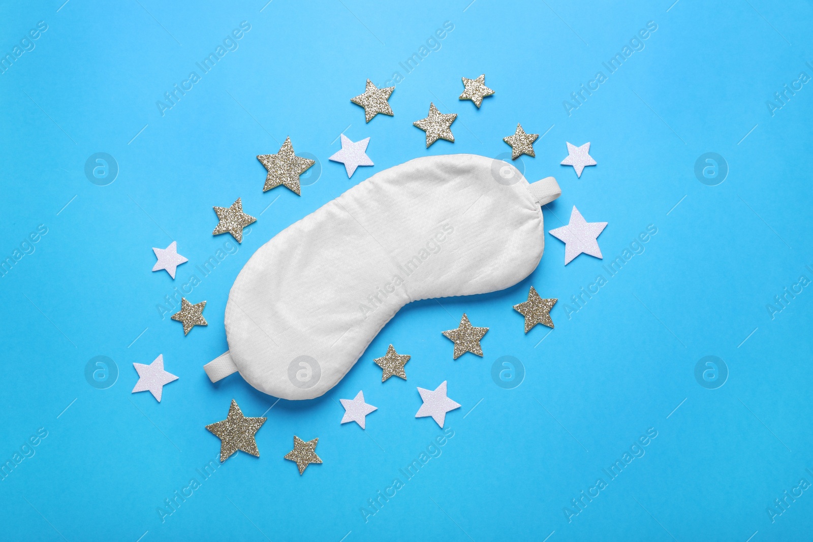 Photo of Soft sleep mask and decorative stars on light blue background, flat lay