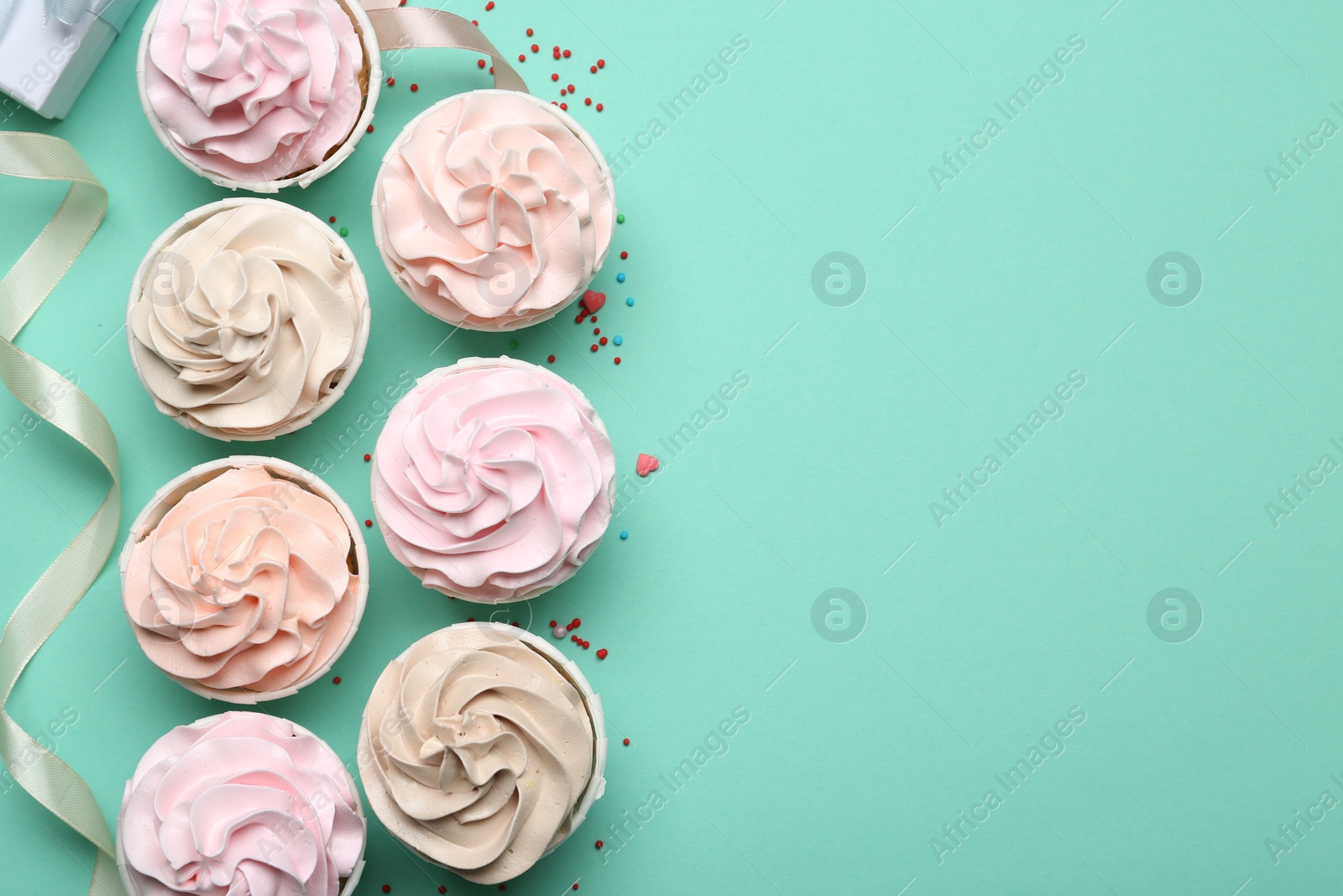 Photo of Delicious birthday cupcakes, ribbon and sprinkles on turquoise background, flat lay. Space for text