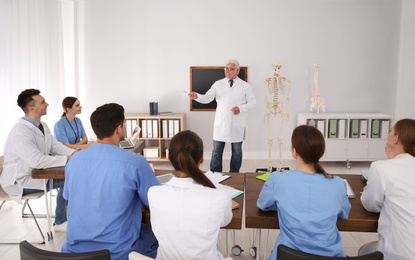 Medical students and professor studying human skeleton anatomy in classroom