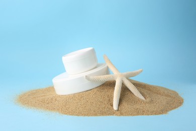 Photo of Jars with cream and starfish on sand against light blue background. Cosmetic products