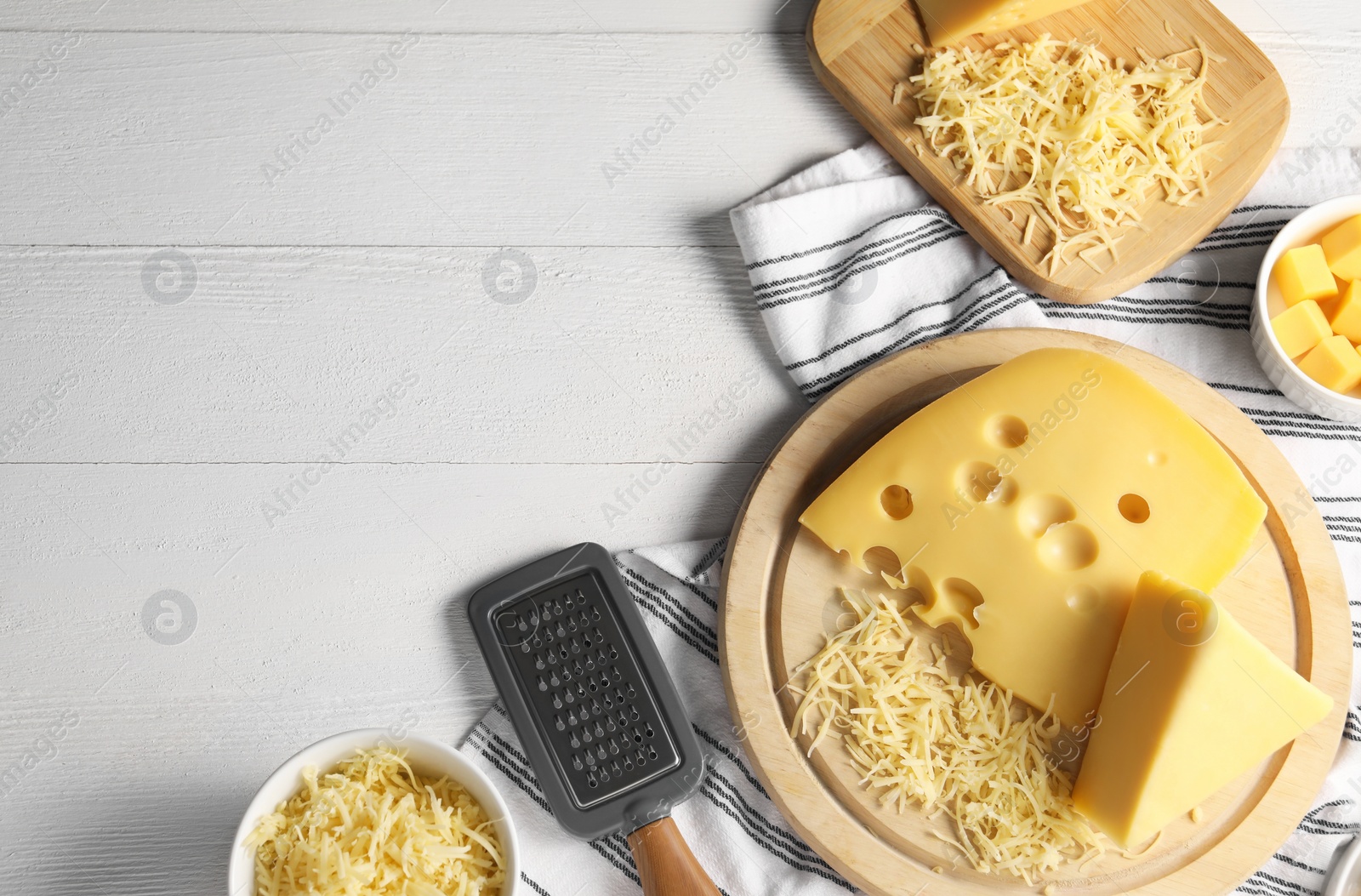 Photo of Grated, cut cheese and grater on white wooden table, flat lay. Space for text