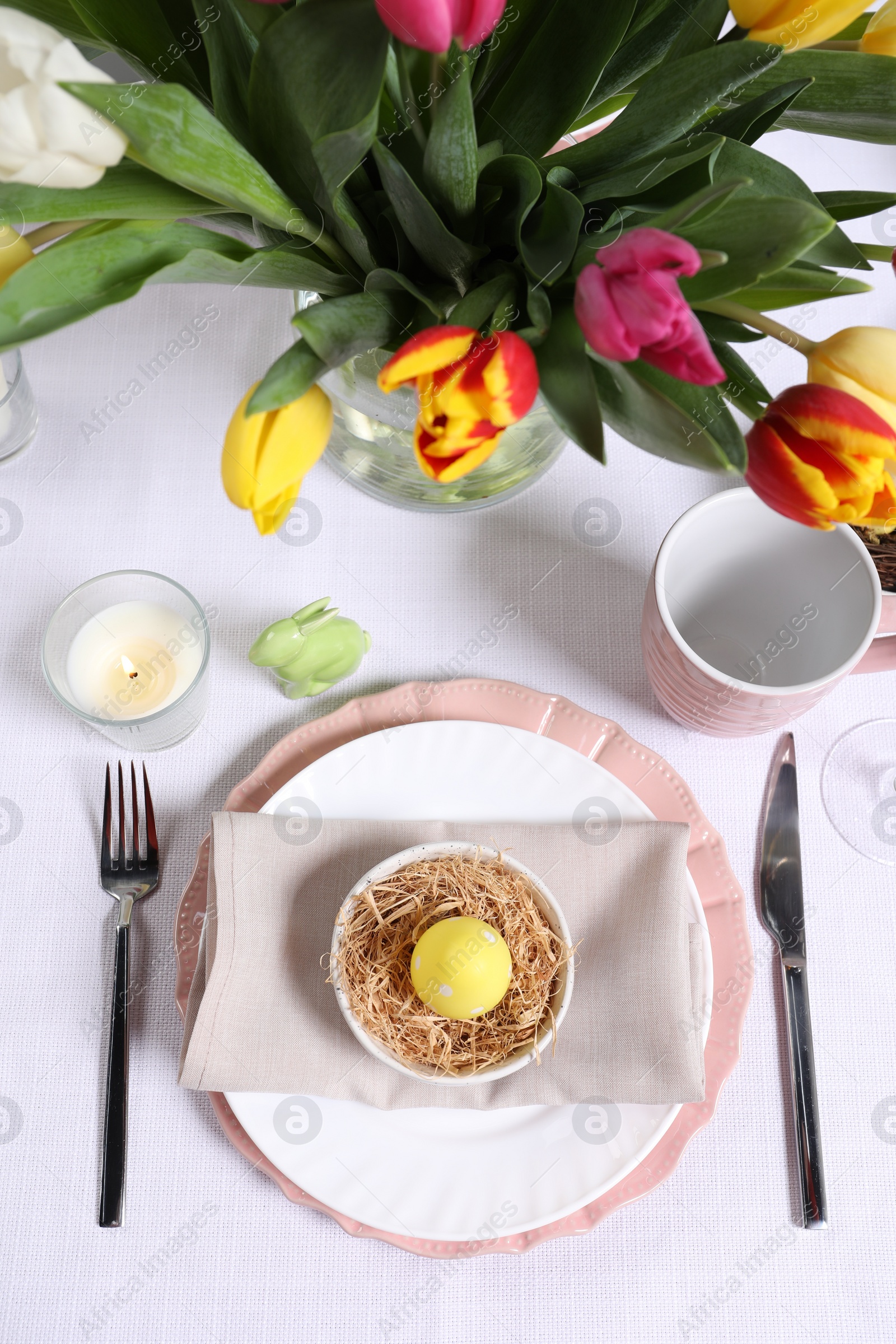 Photo of Festive table setting with painted egg in decorative nest, flat lay. Easter celebration