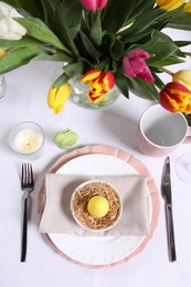 Festive table setting with painted egg in decorative nest, flat lay. Easter celebration