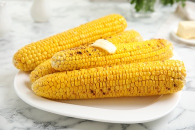 Fresh grilled corn cobs with butter on white marble table, closeup