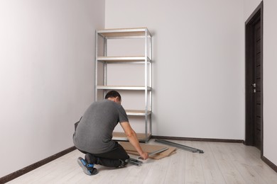 Photo of Worker assembling metal storage shelf in new office room, back view