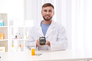 Photo of Pharmacist with payment terminal and pills in drug store