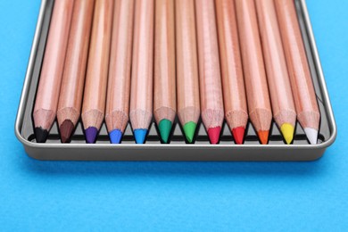 Photo of Box with many colorful pastel pencils on light blue background, closeup. Drawing supplies