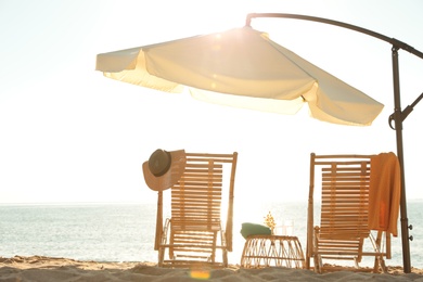 Photo of Wooden deck chairs, outdoor umbrella and beach accessories near sea. Summer vacation