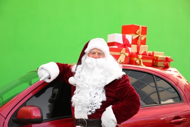 Authentic Santa Claus near car with presents on roof against green background