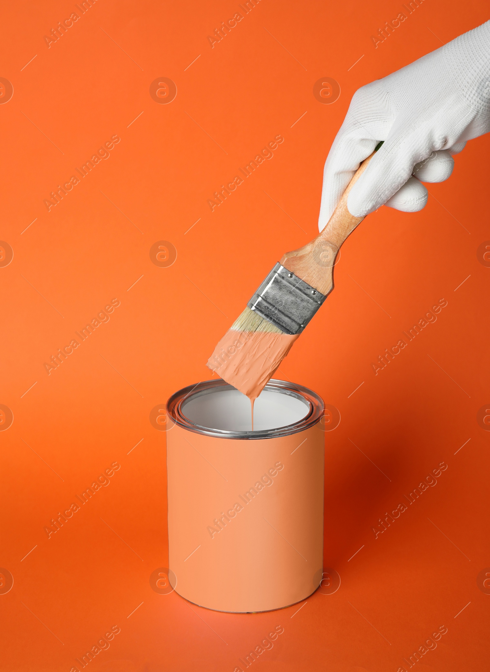 Photo of Person dipping brush into can of paint on orange background