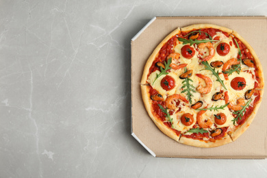 Photo of Delicious seafood pizza  in cardboard box on grey marble table, top view. Space for text