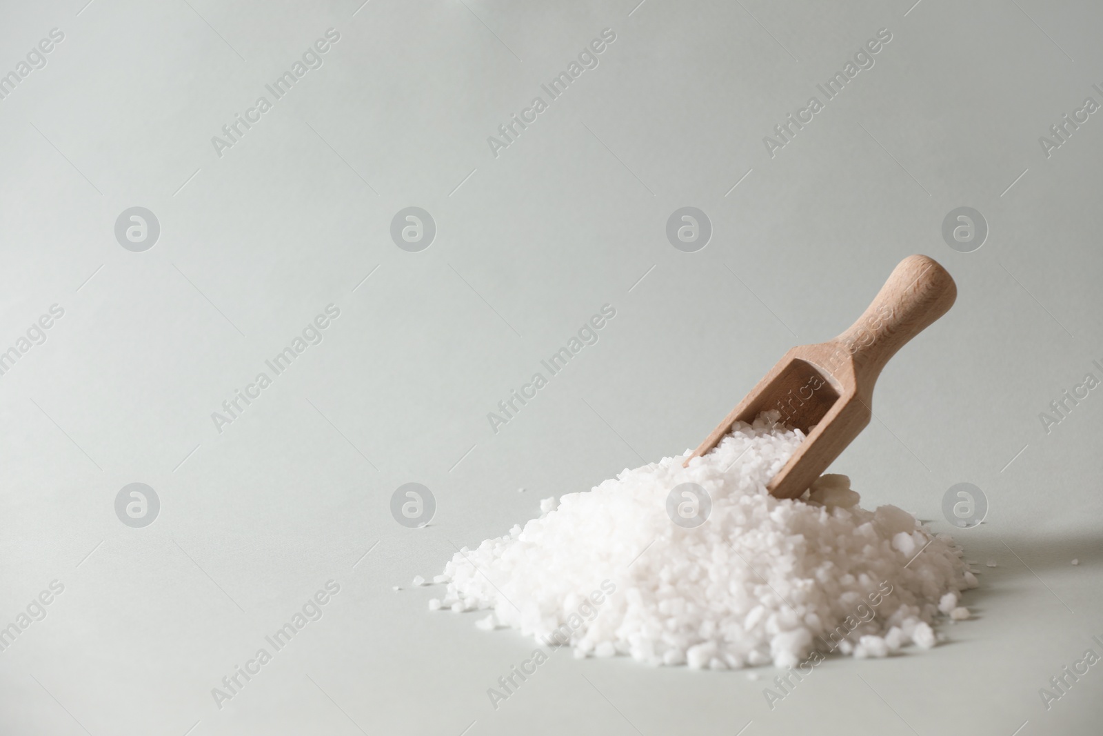 Photo of Organic salt and wooden scoop on light grey background. Space for text