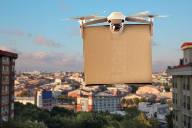 Image of Modern drone with carton box flying above city on sunny day. Delivery service 