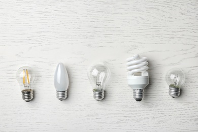 Photo of Set of different lamp bulbs on white wooden background, top view