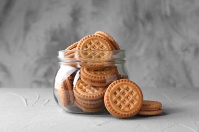 Photo of Tasty sandwich cookies with cream in jar on light grey table
