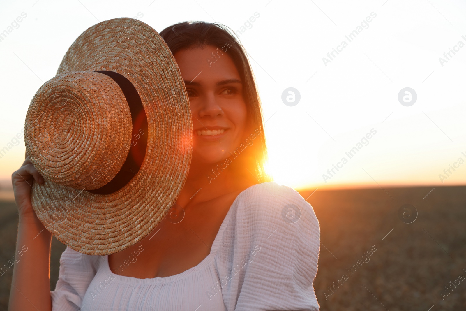 Photo of Beautiful young woman with straw hat in ripe wheat field at sunset, space for text